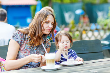 Mother and little adorable kid girl drinking coffee in outdoor c