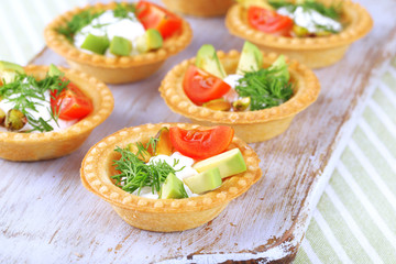 Tartlets with greens and vegetables with sauce on tray on table
