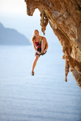 Tired female rock climber resting while hanging on rope