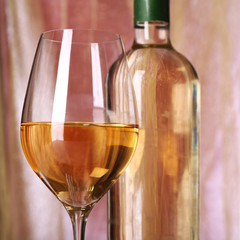 Wine bottle and wineglass with white wine on bright background