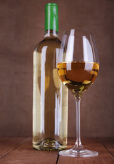 Wine bottle and wineglass with white wine on wooden background