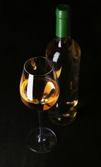 Wine bottle and wineglass with white wine on dark background
