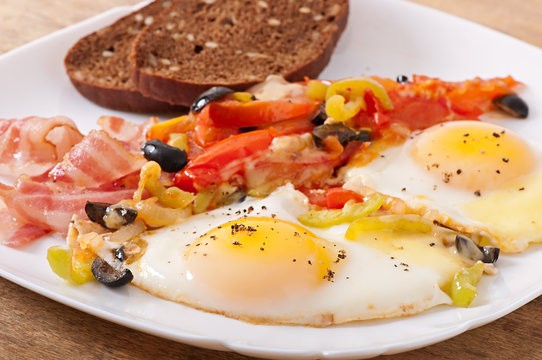 Breakfast - fried eggs with bacon, tomatoes, olives and cheese