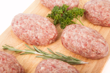 fresh uncooked patties on a wooden board with rosemary and parsl