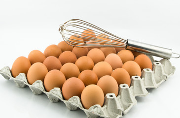 egg tray and hand whisk on white background