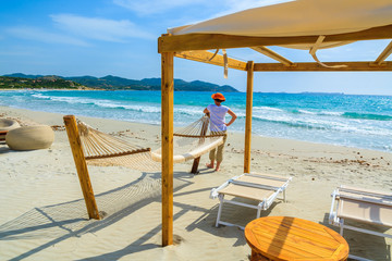 Young woman standing against hammock on beach, Sardinia island