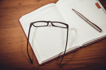 pen, notebook and glasses at brown table