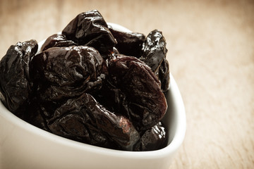dried plums prunes in white bowl on wooden table