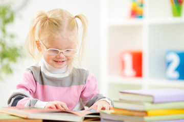 Funny child in eyeglases reading book at home