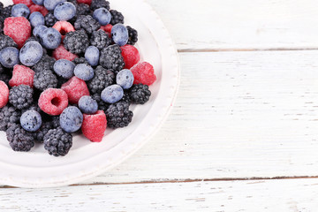Iced berries on plate, on color wooden background