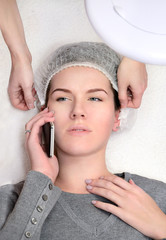 Woman in spa salon waiting for injections and talkig on phone