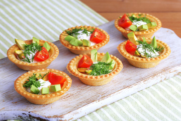 Tartlets with greens and vegetables with sauce on tray on table