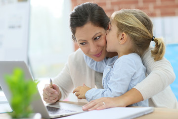 Little girl giving kiss to her mom while working from home