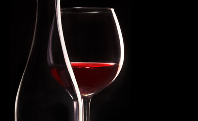 A glass of red wine with a bottle. Isolated on black.