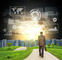 Businessman walks on road. Rear view. Buildings, grass field and