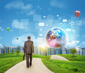 Businessman walks on road. Rear view. Buildings, grass field and