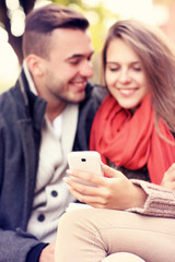 Blurry portrait of a young couple on a bench with smartphone in