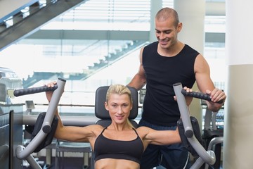Fototapeta na wymiar Trainer assisting woman on fitness machine at gym