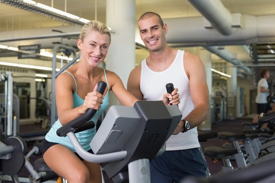 Male trainer assisting woman with exercise bike at gym