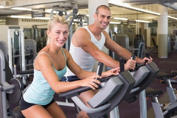 Fototapeta na wymiar Fit young couple working on exercise bikes at gym