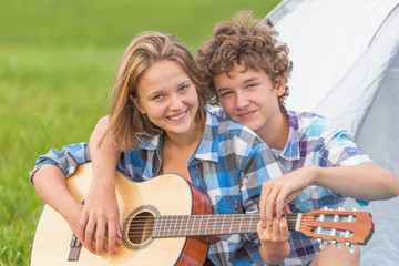 Teenage boy and girl near the tent playing a guitar outdoors