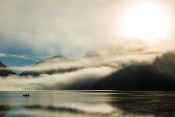 mystic dust over austrian alps lake with fisher boat and fog