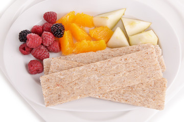 Slices of fruits with berries and crispbreads on plate close up
