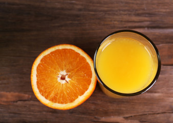 Glass of orange juice and fresh orange on wooden background