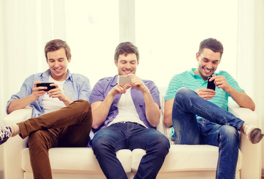 smiling friends with smartphones at home