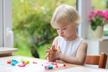 Blonde toddler girl making cookies from plasticine