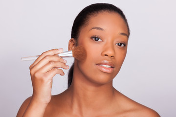 Obraz na płótnie Canvas Young beautiful african woman applying makeup - Black people