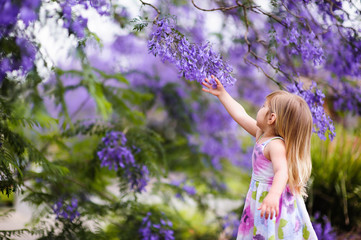happy little girl has a fun in blossom jacaranda garden