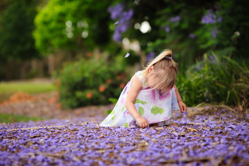 Cute happy little girl in blooming park. Beautiful Jacaranda