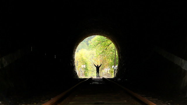 Person finds way out, stands happy, end of tunnel light