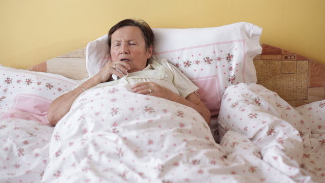 Ill senior woman coughing in bed.
