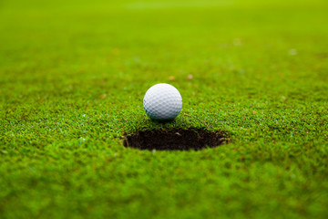 Golf ball on green meadow. golf ball on lip of cup