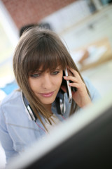 Young woman talking on smartphone in front of desktop