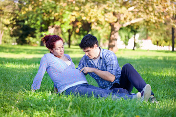 Naklejka na ściany i meble Pregnant couple relaxing in autumn park