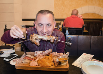 Мужчина в ресторане  держит рюмку водки и ест мясо на вертеле