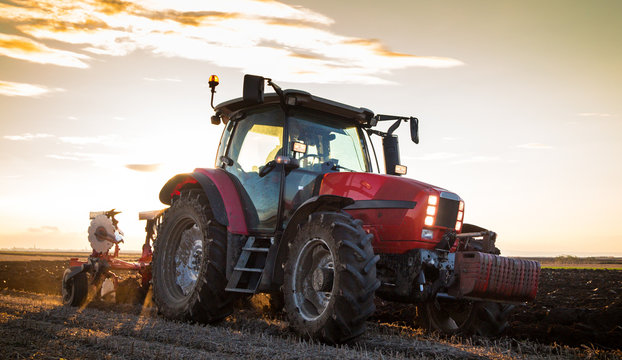 Farmer plowing stubble field with red tractor at sunset