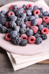 Iced berries on plate, on color wooden background