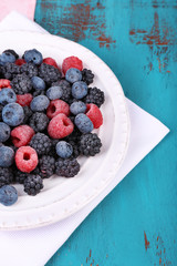 Iced berries on plate, on color wooden background