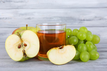 glass of juice with fresh grape and apples on grey wooden table