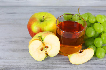 glass of juice with fresh grape and apples on grey wooden table
