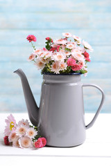 Beautiful flowers in pitcher on table on light blue background