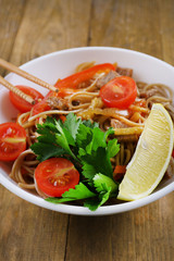 Chinese noodles with vegetables and roasted meat in bowl