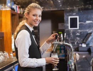 Barmaid pulling a glass of beer while looking at camera
