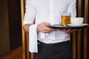 Smiling waiter holding tray with coffee cup and pint of beer