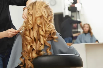 Rolgordijnen Blond krullend haar. Kapper doet kapsel voor jonge vrouw i © puhhha