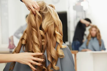 Rolgordijnen Blond krullend haar. Kapper doet kapsel voor jonge vrouw i © puhhha